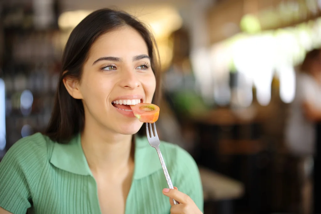 Femme souriante mangeant une tomate avec une fourchette au restaurant.
