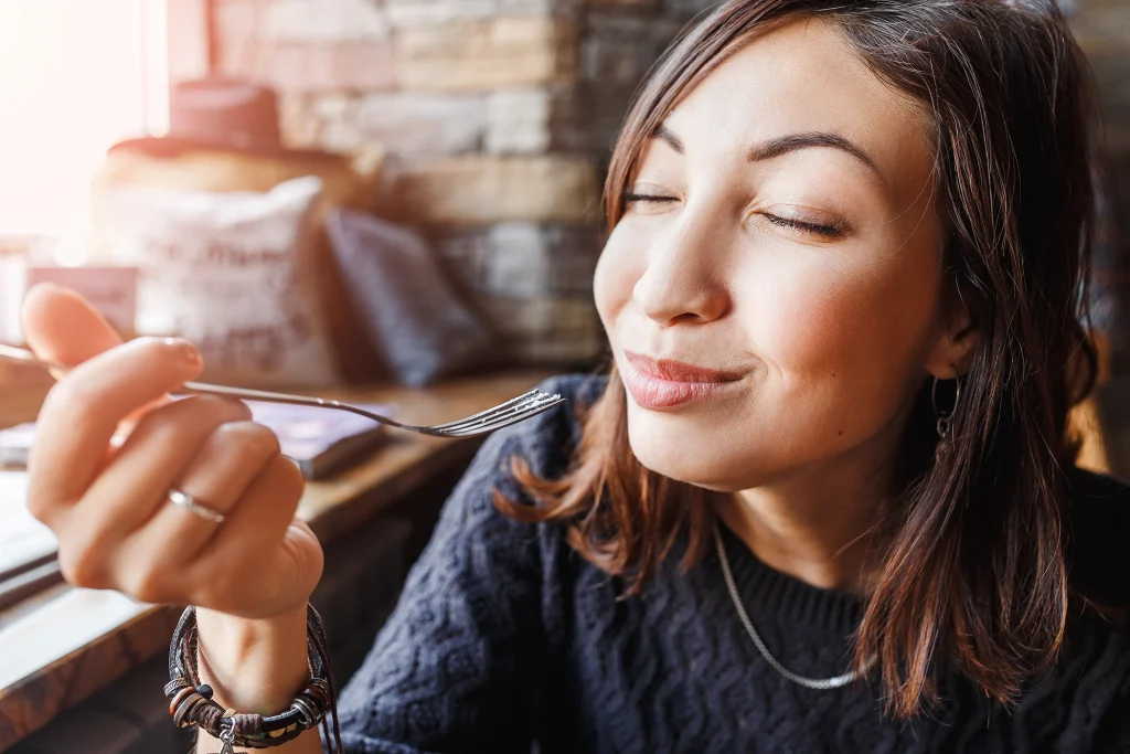 Femme savourant une bouchée les yeux fermés, attentive aux sensations et au plaisir de manger.